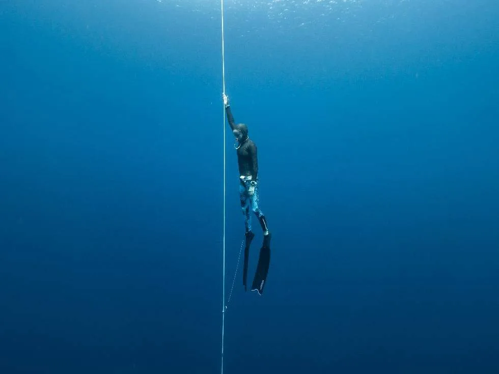 Freediver pulling hand over hand along the dive line in the deep blue off Koh Tao